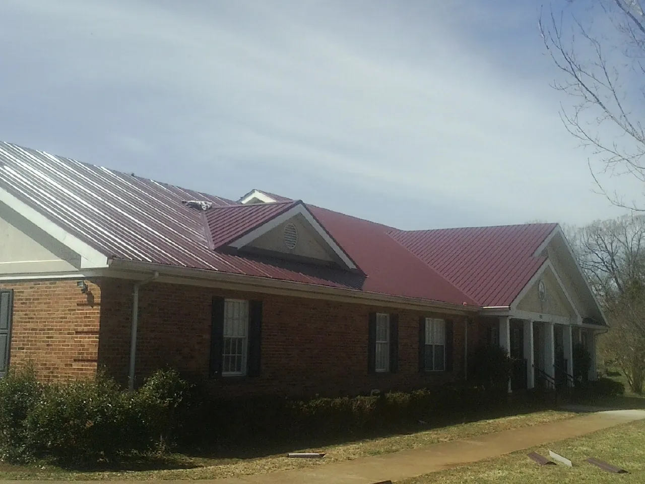 Red metal roof with gabled entries on a long brick building, from a Hail Damage Roof Repair job in Okahumpka