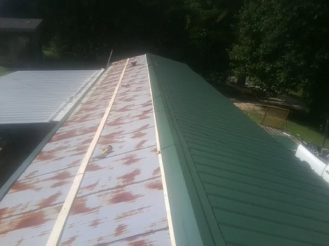 Old rusted panels beside newly installed green metal roofing — Wind Damage Roof Repair by Roofing Brothers in Okahumpka