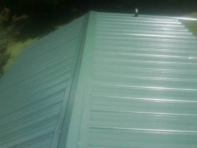 New green metal panels meeting at the ridge of a roof — Flat Roof Repair work by our crew in Okahumpka