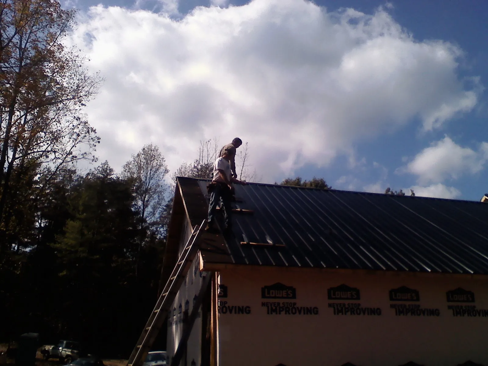 Roofer fastening dark metal panels high against a cloudy sky, from a Roof Inspection job in Okahumpka