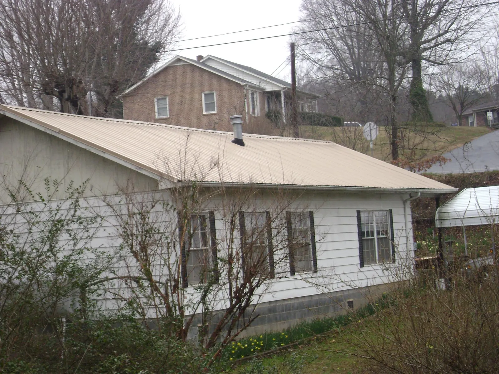 Tan metal roof on a white sided house set into a hillside — Commercial Roofing by Roofing Brothers in Okahumpka